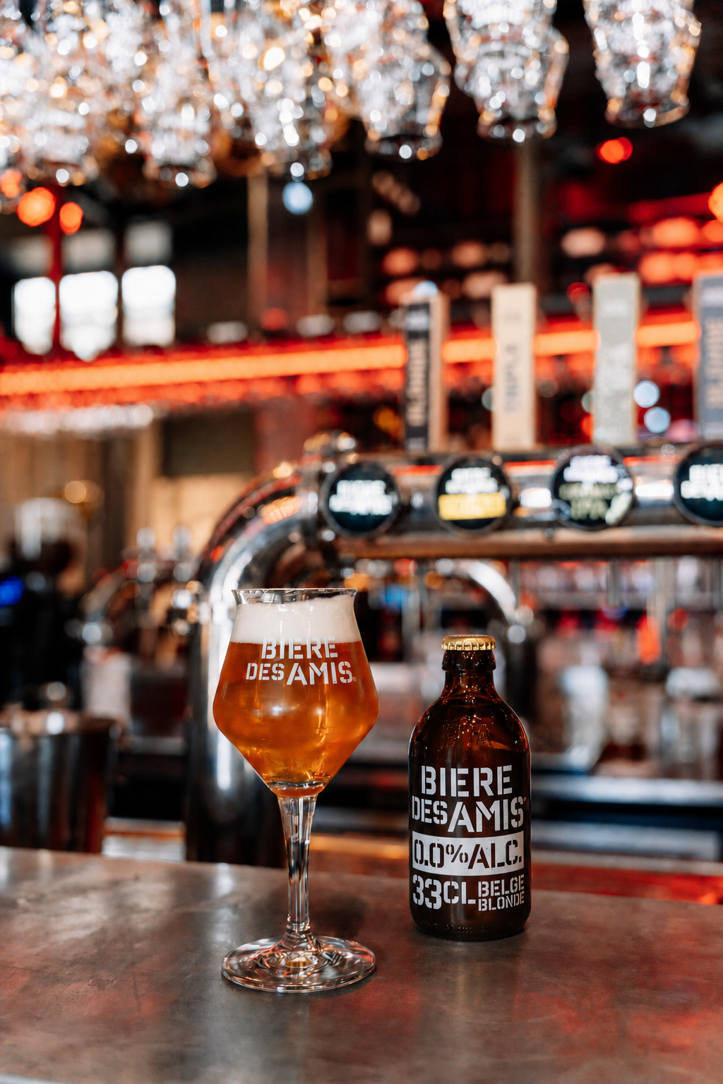 BDA 0.0_retouched 9:16 bouteille de bière des amis blonde 0.0% posée à côté d'un verre sur pied rempli, dans un beau bar à bières